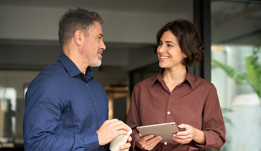 Two colleagues speaking face-to-face in a workplace setting, smiling during a conversation