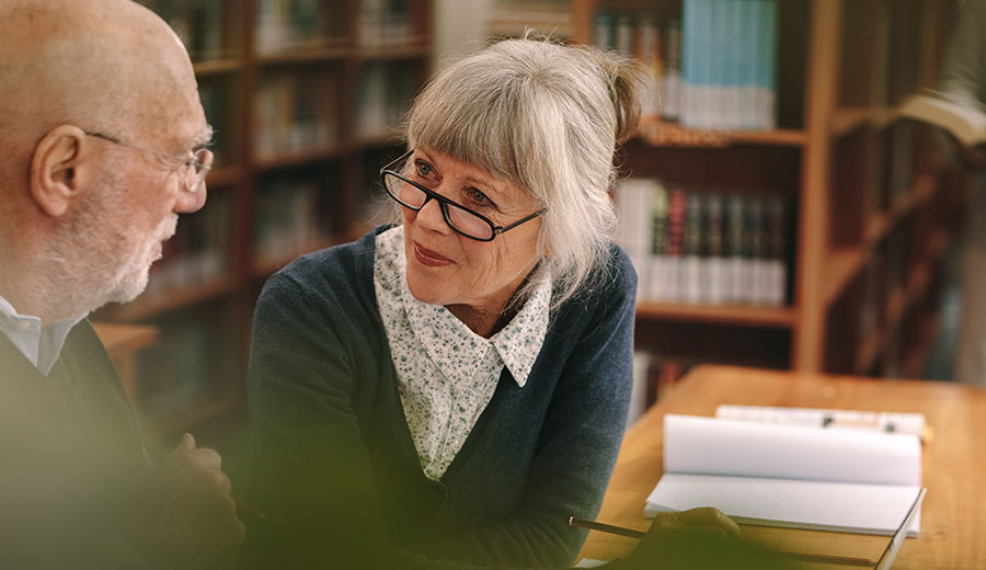 Senior leader in conversation, listening attentively during a one-to-one discussion in an office with bookshelves in the background